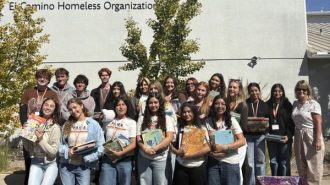 A group holding donated books in front of the El Camino Homeless Organization building in Atascadero